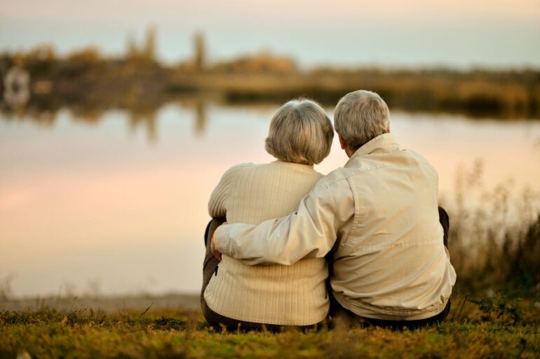 Senior couple with arms around each other, looking at water