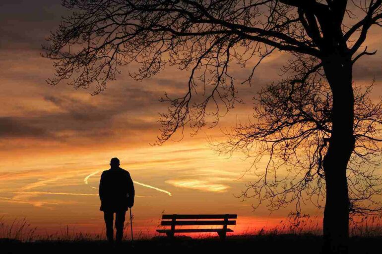 Silhouette of a man standing alone next to a park bench watching the sunset - 3 Ways Avoiding Unwanted Sound Can Improve Your Health