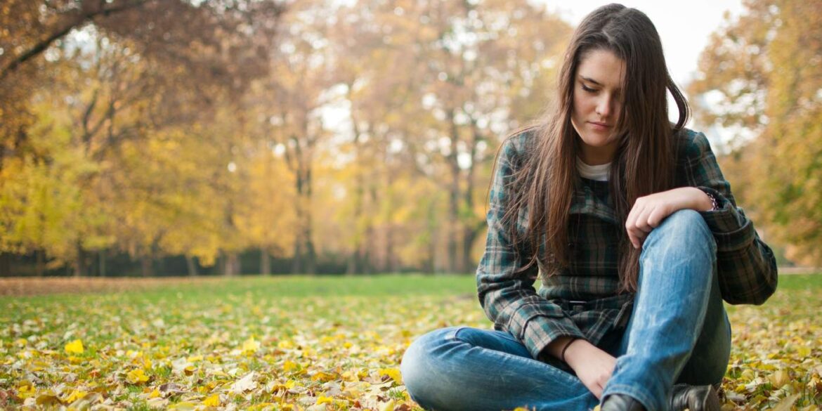 Sad woman sitting outdoors on leaves