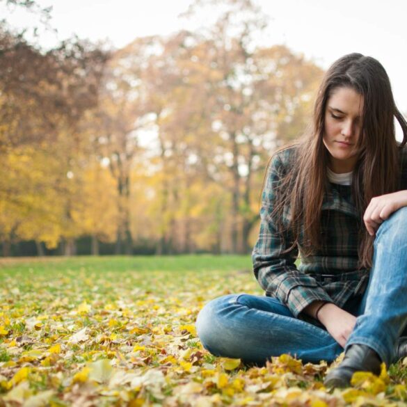 Sad woman sitting outdoors on leaves
