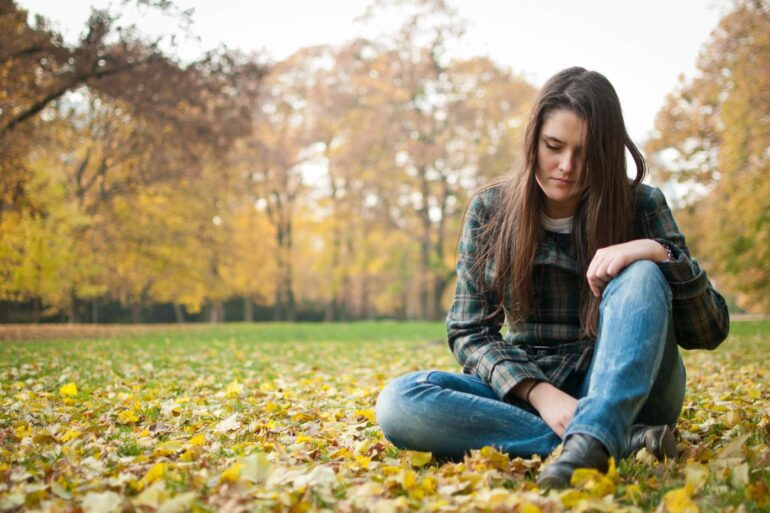Sad woman sitting outdoors on leaves
