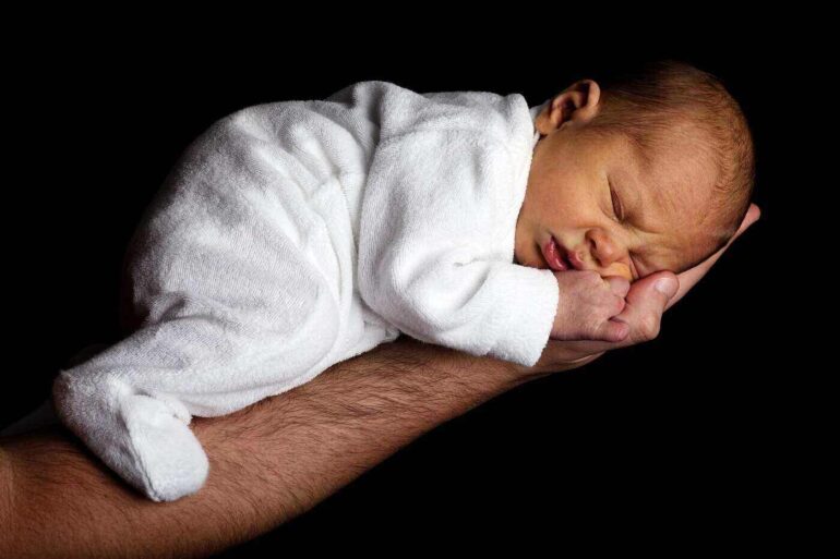 man's extended arm holding a newborn baby