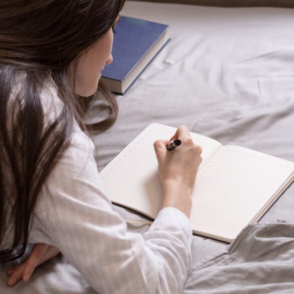 Young woman writing in journal in bed