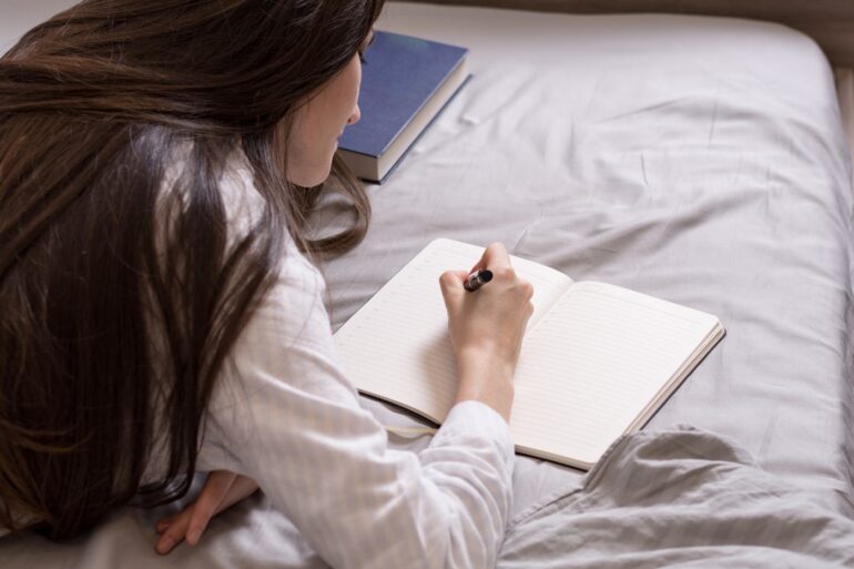 Young woman writing in journal in bed