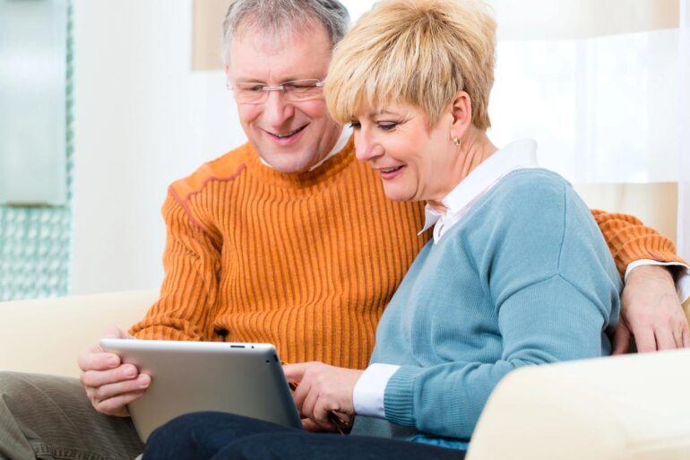 Senior couple looking at tablet together on couch - WRITING AFTER AGE 50: Create a memoir and leave your legacy