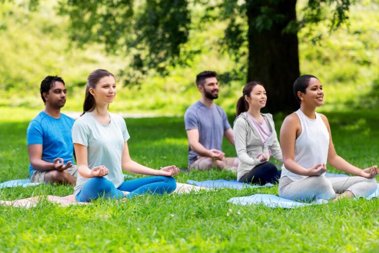 Five people meditating on grass outdoors