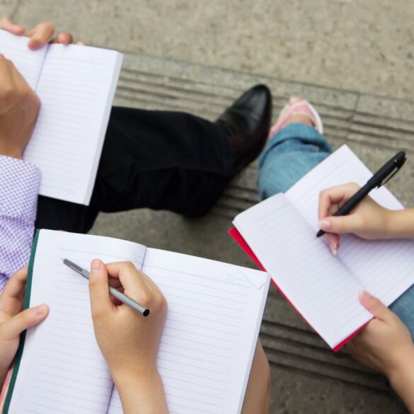 Three people with open notebooks, ready to write - Share Your Story and the Writing Gods Won't Let You Fail