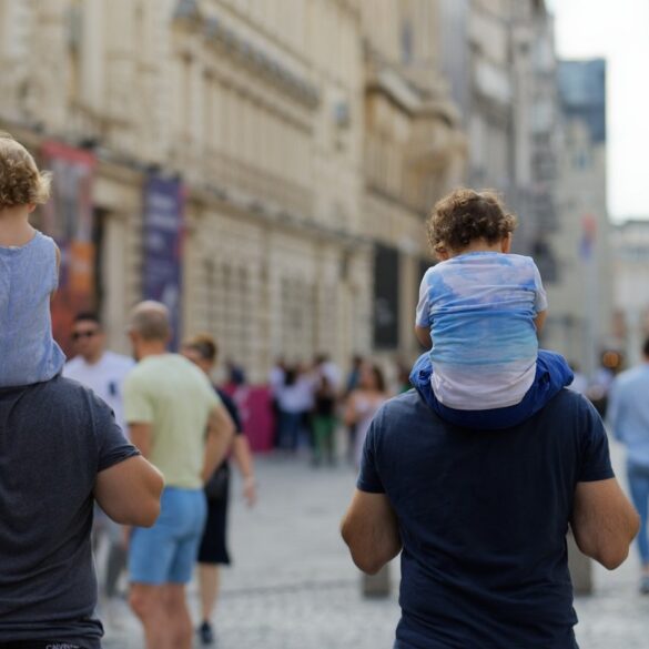 Two dads with kids on shoulders walking down crowded street - Live Responsibly or Destroy Ourselves: The Choice Is Ours