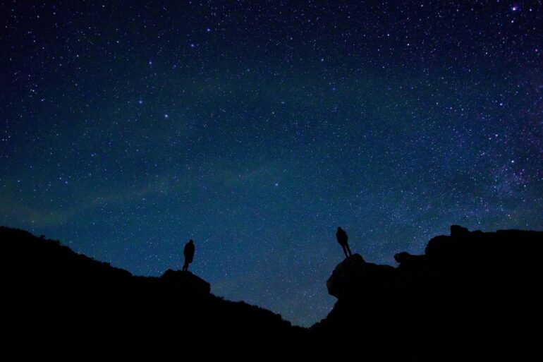 Two silhouettes looking up at night sky from rocky terrain - Dump Your Baggage and Connect With Mind, Spirit and Universe