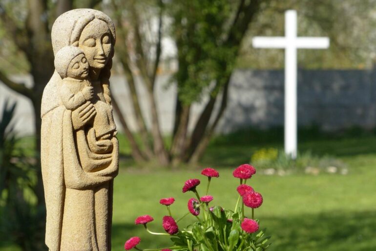 Statue of Mary holding Baby Jesus next to cross - Reflections on Motherhood, Mindfulness Faith and Grace