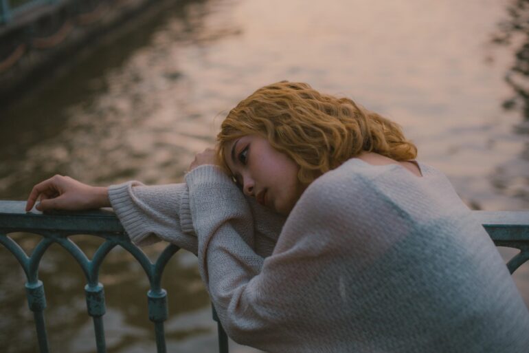 Sad woman with head laying on side of bridge - An Induced Disease: How to Perceive Panic and Stress