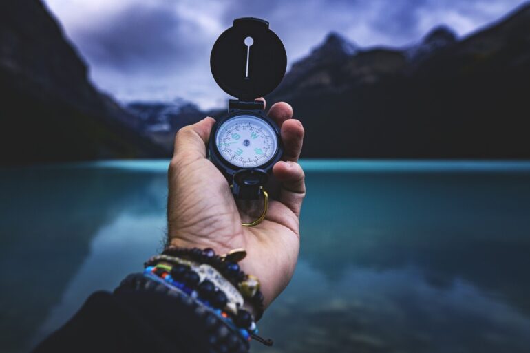 Man holding compass in hand next to mountains and lake - The Body’s Subtle Language: Why Is It Such a Big Deal?