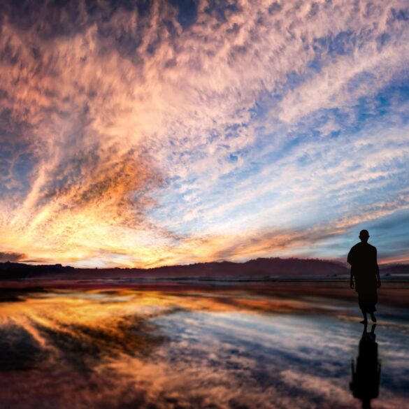 Buddhist monk walking on beach at sunset