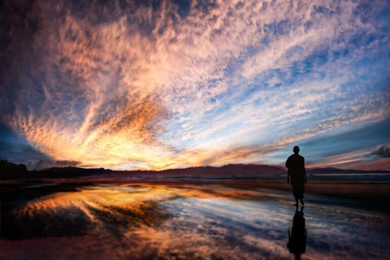 Buddhist monk walking on beach at sunset