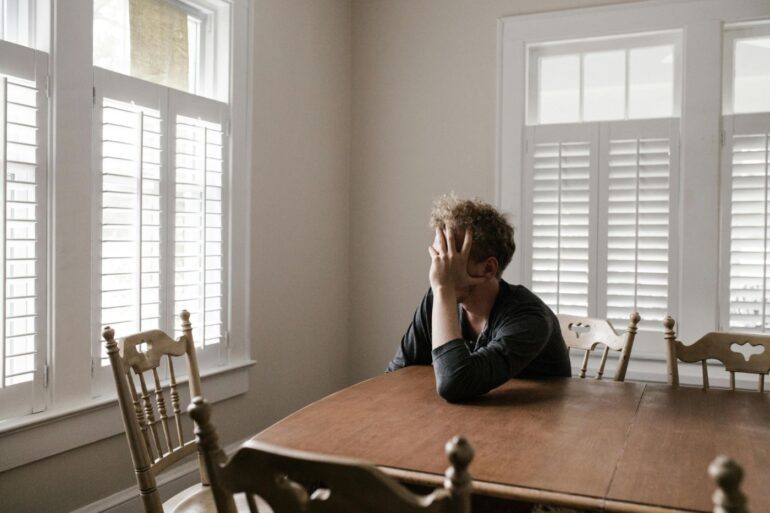 Confused man leaning on wooden table - Gaslighting: What It Is and 3 Effective Ways to Push Back
