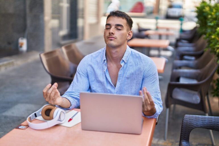 Man meditating at computer outside coffee shop - Buddhist Principles: 5 Valuable Ways to Add Them to Your Day