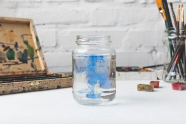 Glass jar full of blue paint next to paintbrushes on table - Take Stock of Your Precious Life: An Inspiring Fiction Story