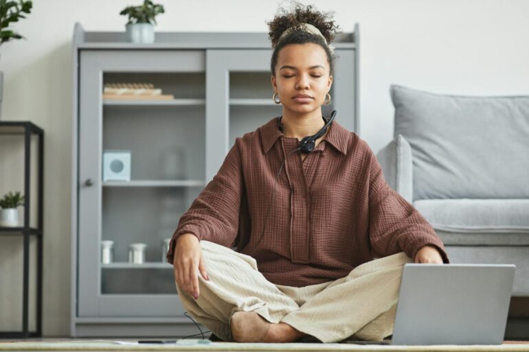 Seated woman, meditating in front of laptop at home - Accountability: How Meditation Groups Help You Stay Mindful