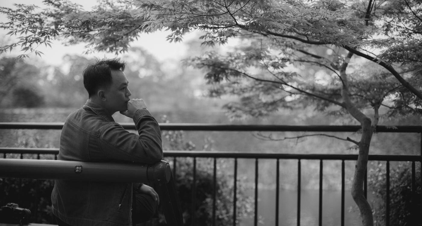 Young man sitting pensively on bench next to tree, looking at water - Understand Your Mind and Honour Its Value