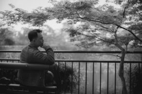 Young man sitting pensively on bench next to tree, looking at water - Understand Your Mind and Honour Its Value