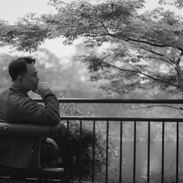 Young man sitting pensively on bench next to tree, looking at water - Understand Your Mind and Honour Its Value