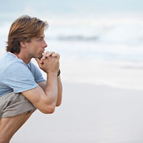 Man crouching pensively on beach - Mindfulness Practice: The Most Important Work You’ll Ever Do