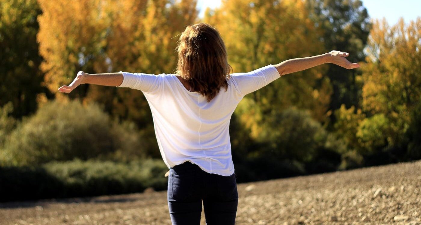 Back view of happy woman with outstretched arms in field - 5 Simple Ways to Be Compassionate Towards Yourself