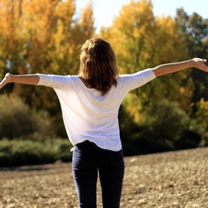 Back view of happy woman with outstretched arms in field - 5 Simple Ways to Be Compassionate Towards Yourself