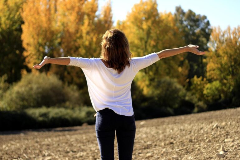 Back view of happy woman with outstretched arms in field - 5 Simple Ways to Be Compassionate Towards Yourself