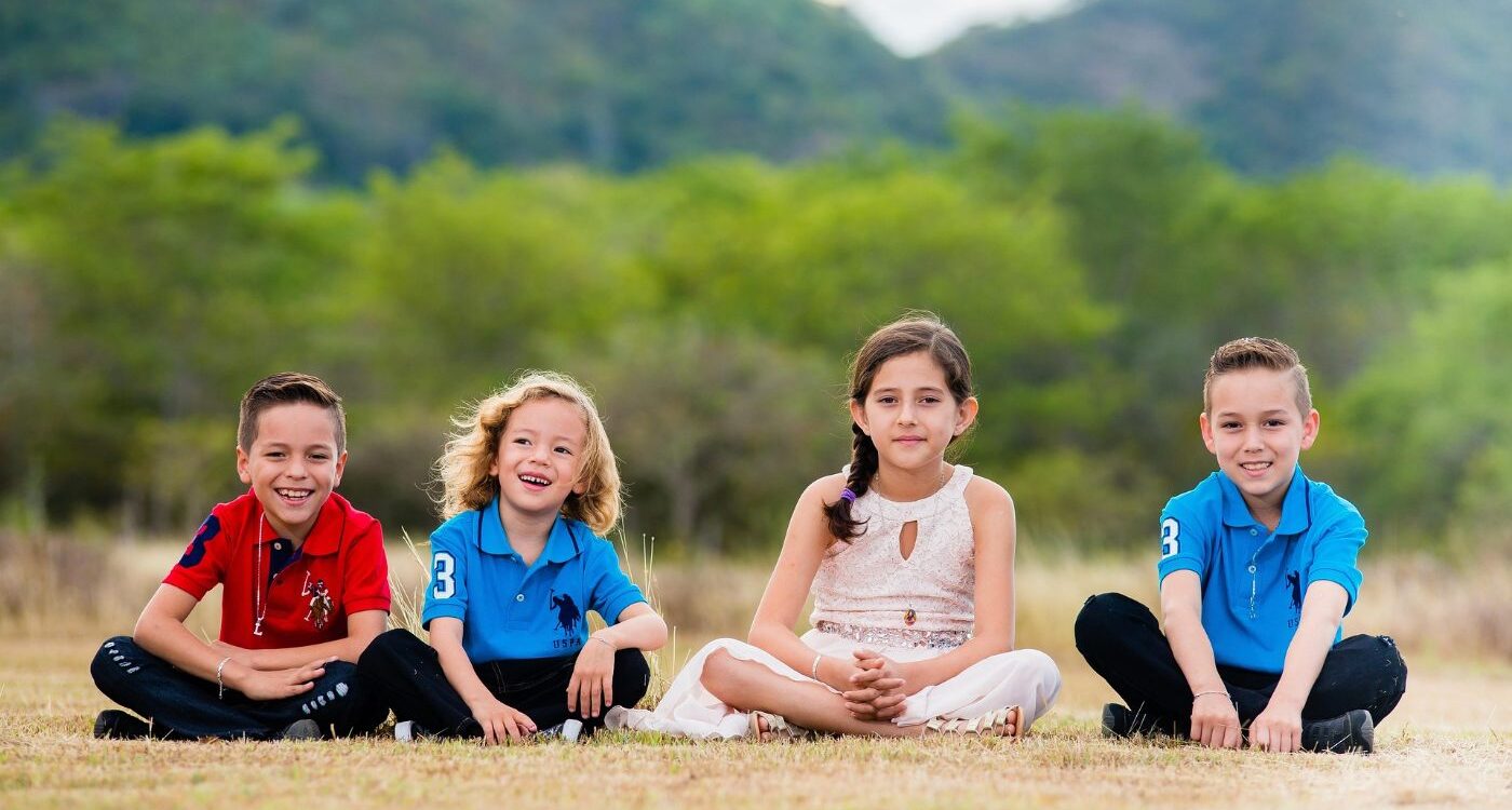 Four happy young kids sitting on ground outdoors - Positive Psychology: Why It’s So Important for Kids