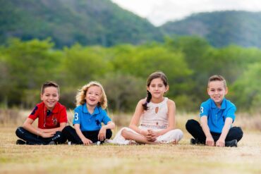 Four happy young kids sitting on ground outdoors - Positive Psychology: Why It’s So Important for Kids