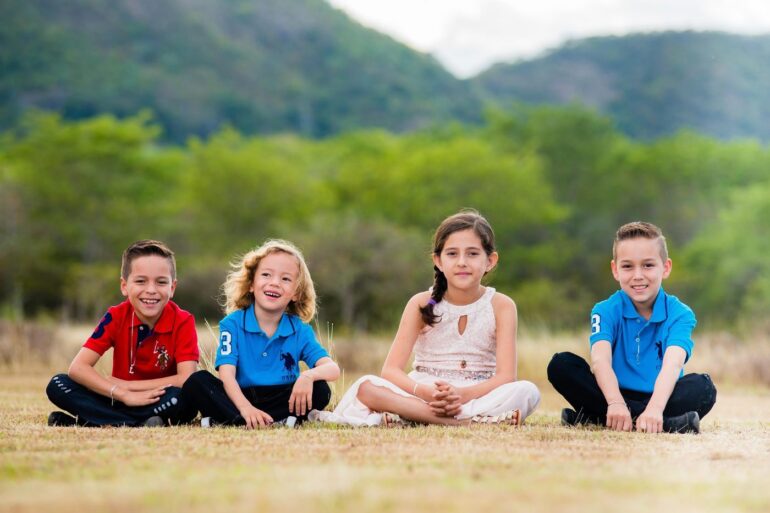 POSITIVE PSYCHOLOGY AND CHILDREN: Why it's important inside and outside of school 13 Four happy young kids sitting on ground outdoors - Positive Psychology: Why It’s So Important for Kids