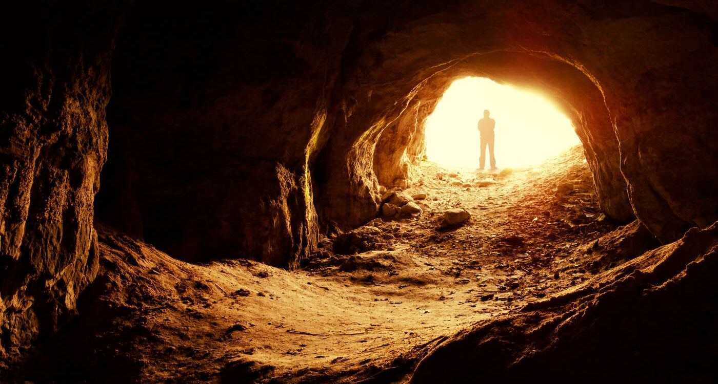 Silhouette of man standing at illuminated opening of cave - Create Your Own Meaningful Grief Ritual in 3 Stages