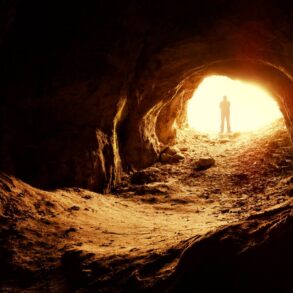 Silhouette of man standing at illuminated opening of cave - Create Your Own Meaningful Grief Ritual in 3 Stages