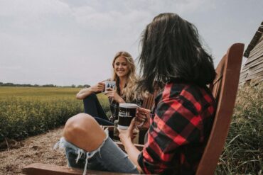 Two young female friends drinking coffee on chairs outdoors - Healthy Self-Alignment: How Mindfulness Can Lead You There