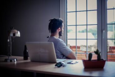 Man relaxing and looking out window while sitting at office desk - Why Mindfulness Matters Greatly in the Modern Workplace