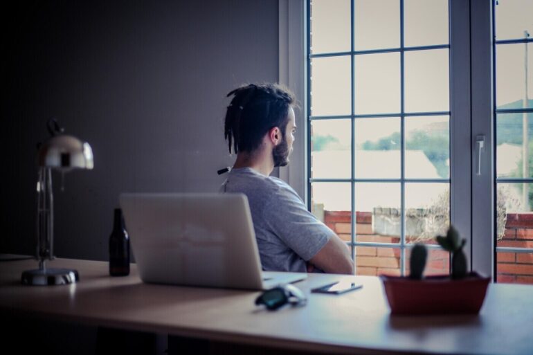 Man relaxing and looking out window while sitting at office desk - Why Mindfulness Matters Greatly in the Modern Workplace