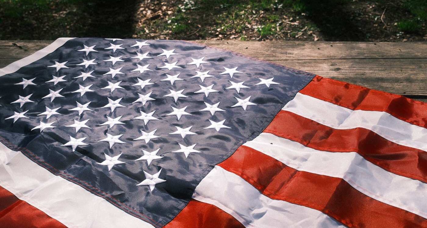 American flag resting on wood with some shadow and some illumination in background - The Dalai Lama and Toni Morrison: Bright Lights on Our Path