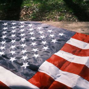 American flag resting on wood with some shadow and some illumination in background - The Dalai Lama and Toni Morrison: Bright Lights on Our Path