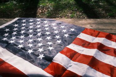 American flag resting on wood with some shadow and some illumination in background - The Dalai Lama and Toni Morrison: Bright Lights on Our Path