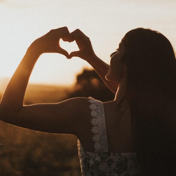 Woman standing alone outdoors making heart shape with hands - An Invitation to Women: Let's Be Gentle With Ourselves Now