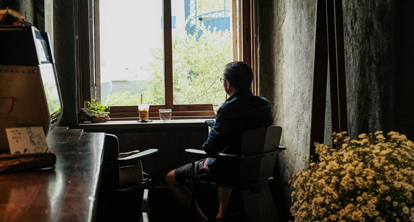 Person looking out window with water and coffee beside them - The Quiet Power of Doing Less Amid a Busy World