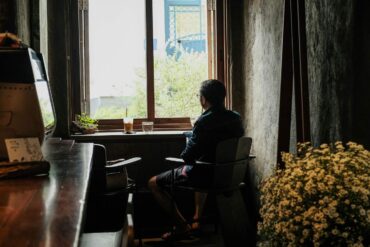 Person looking out window with water and coffee beside them - The Quiet Power of Doing Less Amid a Busy World