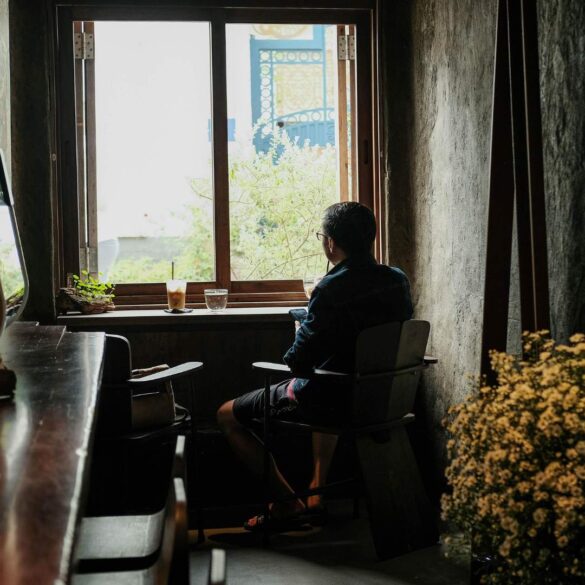 Person looking out window with water and coffee beside them - The Quiet Power of Doing Less Amid a Busy World