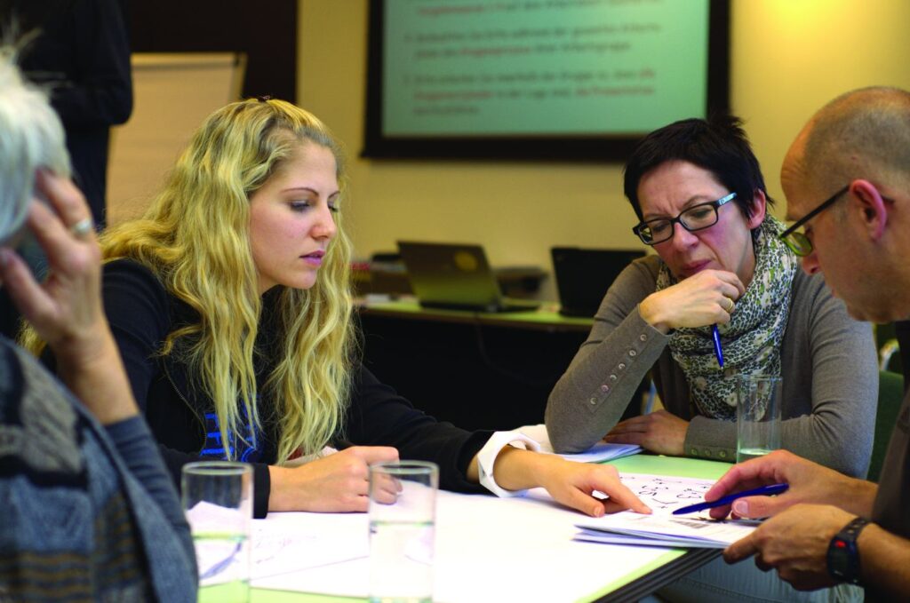 WHAT TEACHING MEMOIR WRITING HAS TAUGHT ME: Holding space for other people's truths 14 Four adults sitting at table working with pens and paper - Why Teaching Memoir Rewards the Students and the Teacher