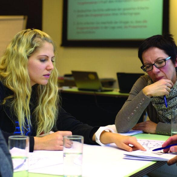 Four adults sitting at table working with pens and paper - Why Teaching Memoir Rewards the Students and the Teacher